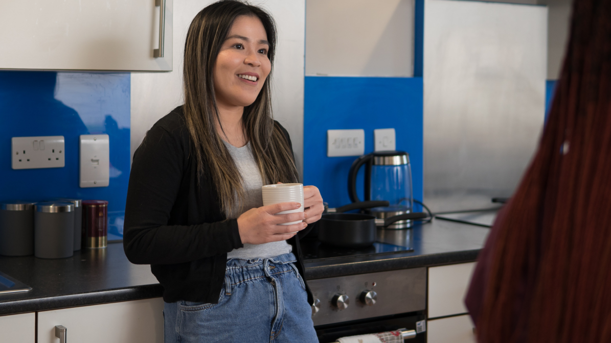 Industry_Marketing_Article_Accommodation_Marketing_Services_Image_1 A student stood in a kitchen, holding a cup of tea and talking
