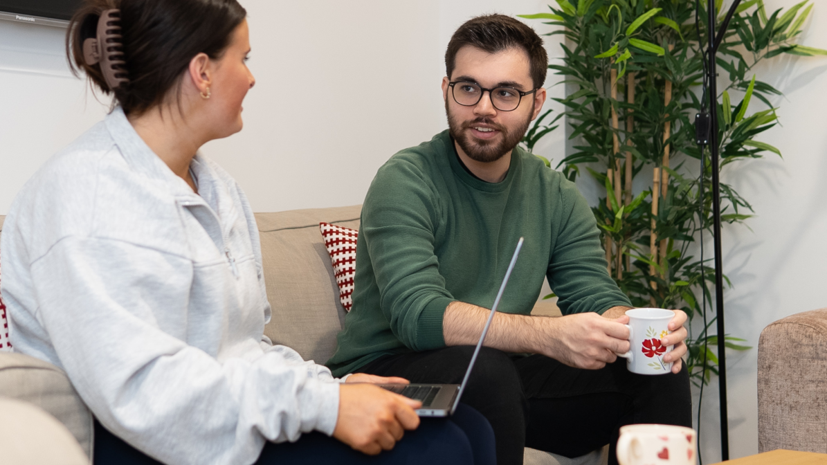 Two people sat together on a couch, focused on a laptop in front of them, sharing a moment of collaboration.