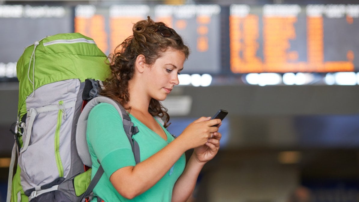Gap year student at station looking on mobile phone
