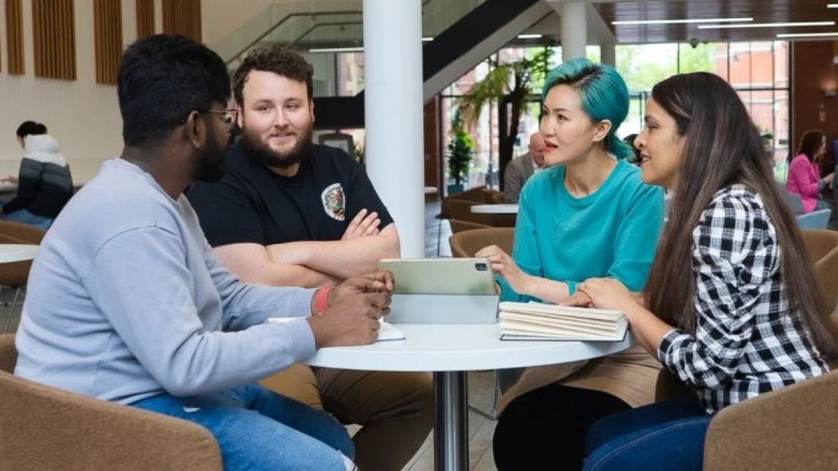 Students with individual needs chatting around a table in uni communal area