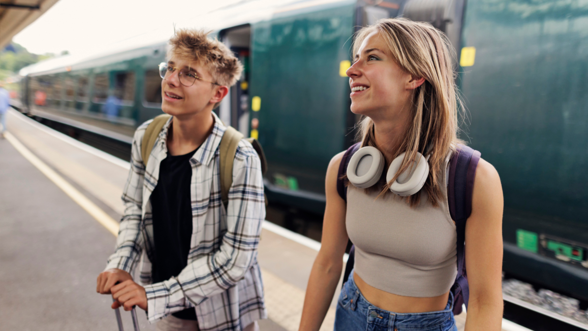 Gap_Years_Image_Box_1_Train_Platform Two gap year students with backpacks and travel gear smiling on a train platform, representing UK 18-year-olds preparing for travel, volunteering, or career experiences. Ideal visual for brands targeting students during their year out through campaigns in education, travel, and youth marketing sectors.