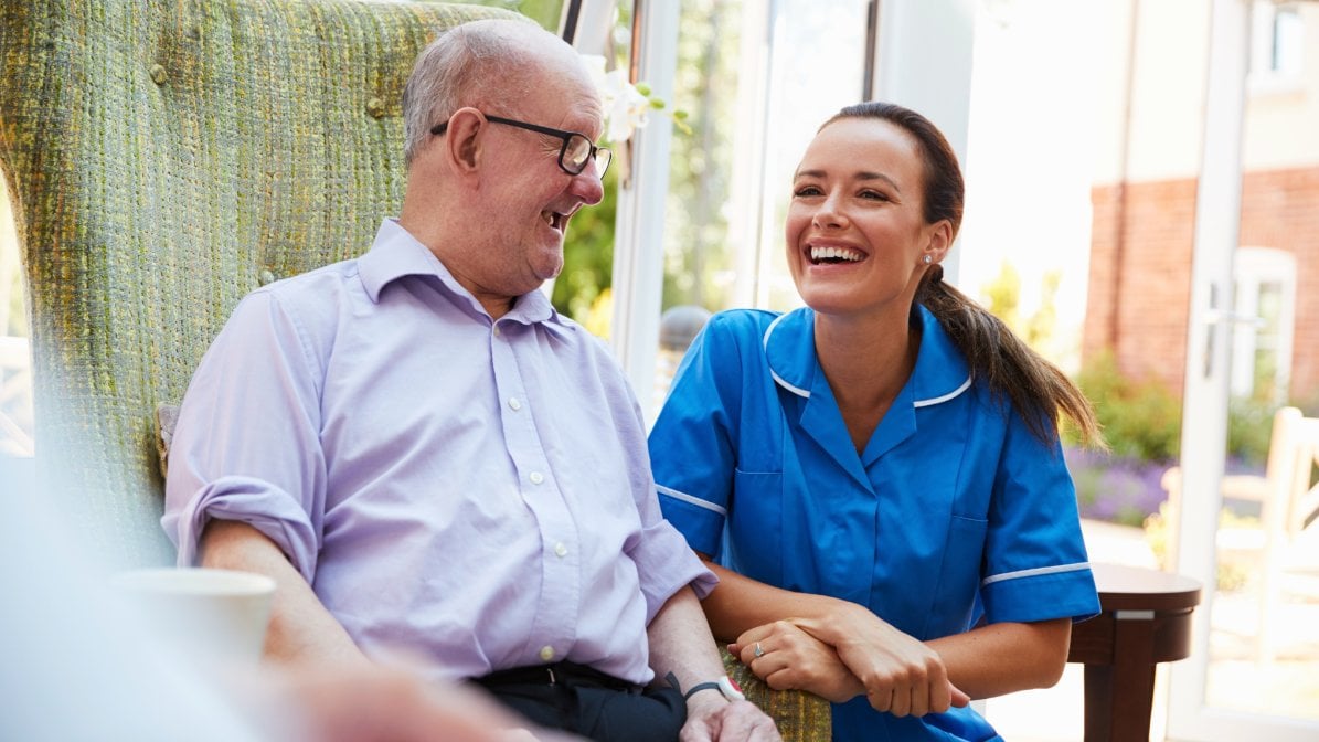 An apprentice nurse laughs with an elderly patient
