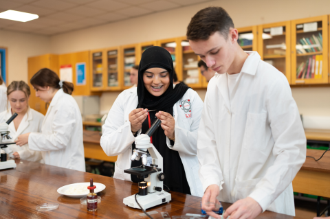A pair of students, both wearing labcoats, conducting a science experiment in a classroom