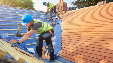 An apprentice helps to tile a roof