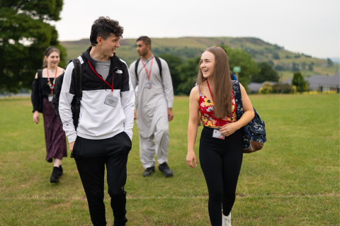 A group of four students, laughing and chatting, walking across a school sports field