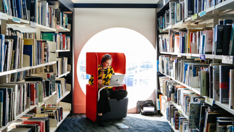 Student sitting by the window working on their laptop in Ravensbourne's library 